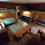 Wood-panelled room, armoire, coffee table, couch, 3 bunk beds, hallway in the background