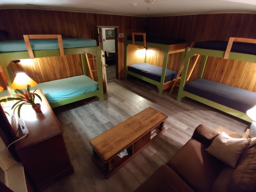Wood-panelled room, armoire, coffee table, couch, 3 bunk beds, hallway in the background