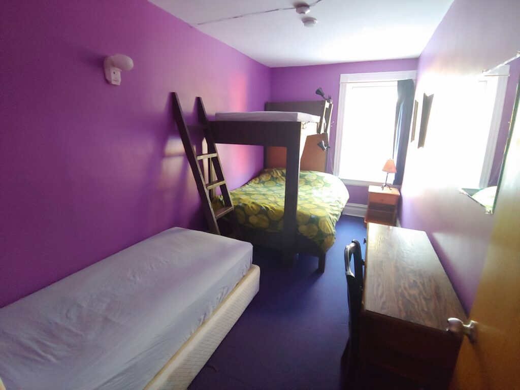 purple room with single bed and bunk bed, desk, night table, lamp, window