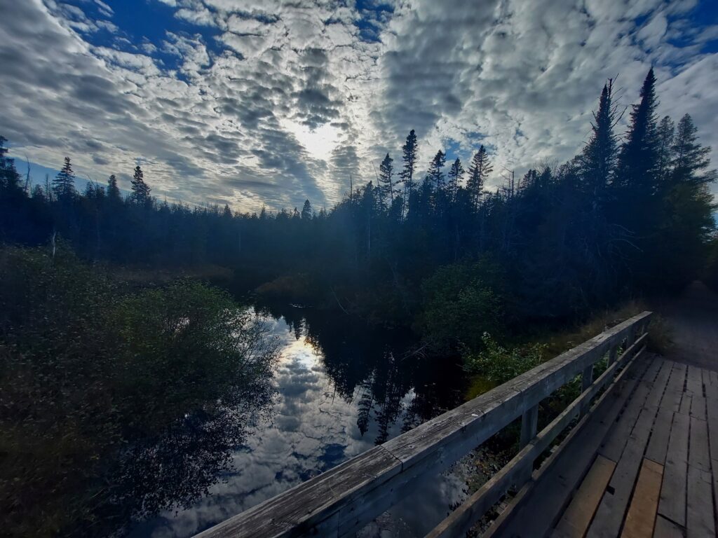 streamers of clouds reflected in creek with wooden bridge