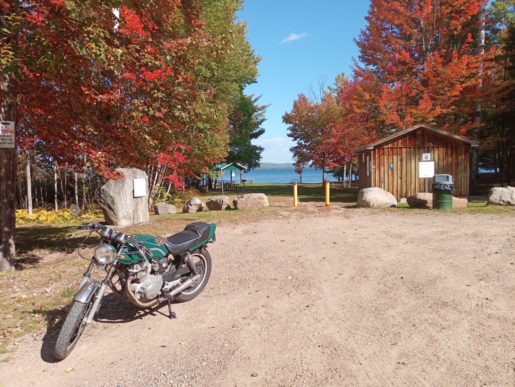 red-leafed trees behind parking lot with motorcycle in front of bark lake