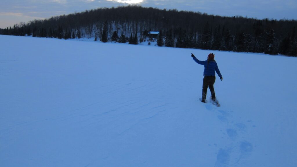 woman snowshoeing on frozen Mitchell lake pointing skyward