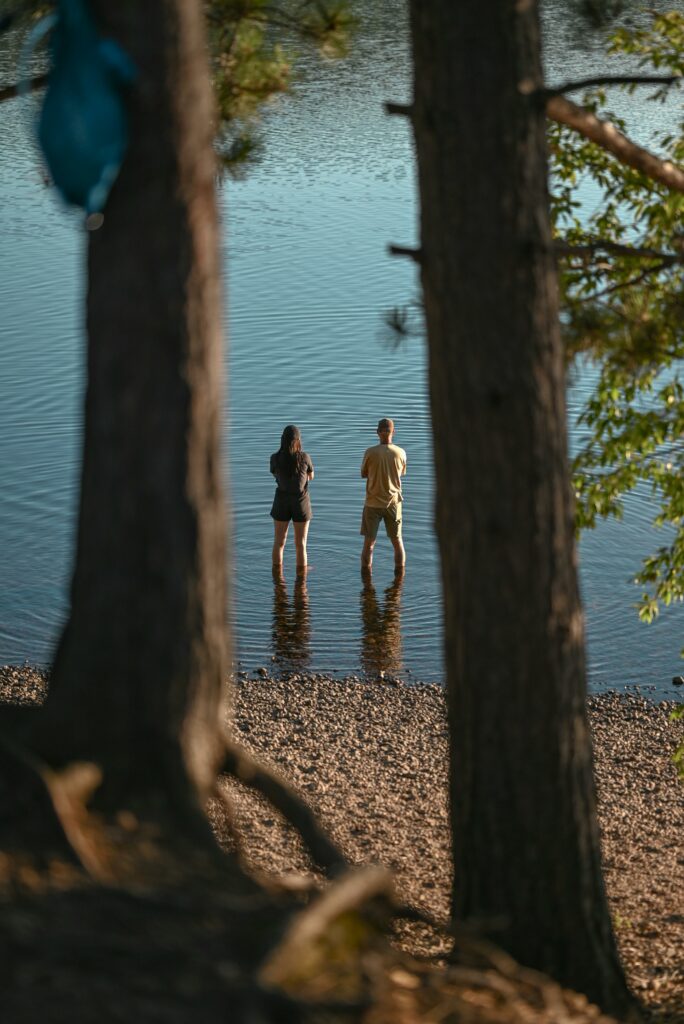Two people standing knee deep in a lake with two trees in the foreground