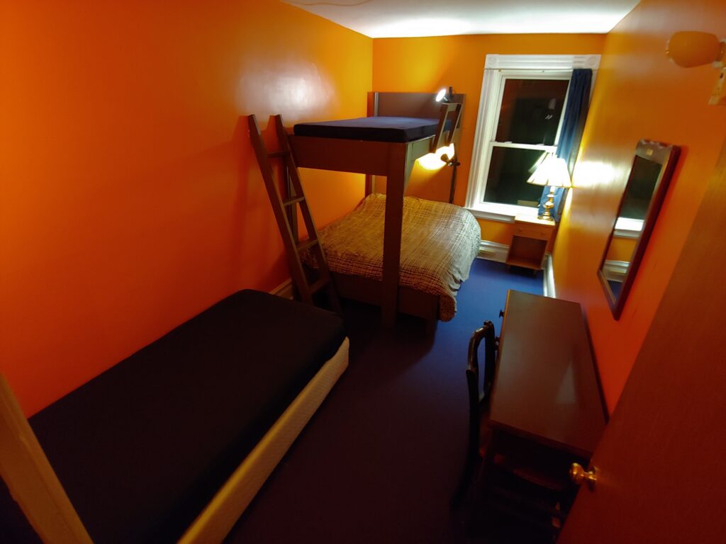 orange room with single bed, bunk bed, desk, lamp