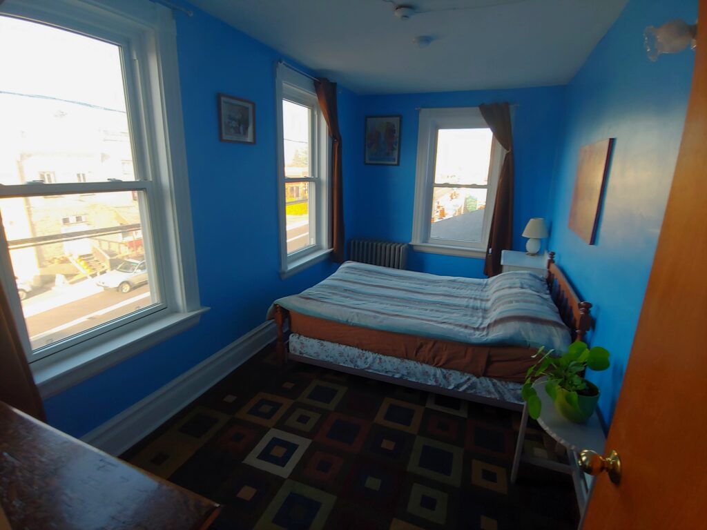 blue room with a double bed, desk & night table - the brown carpet has squares within squares