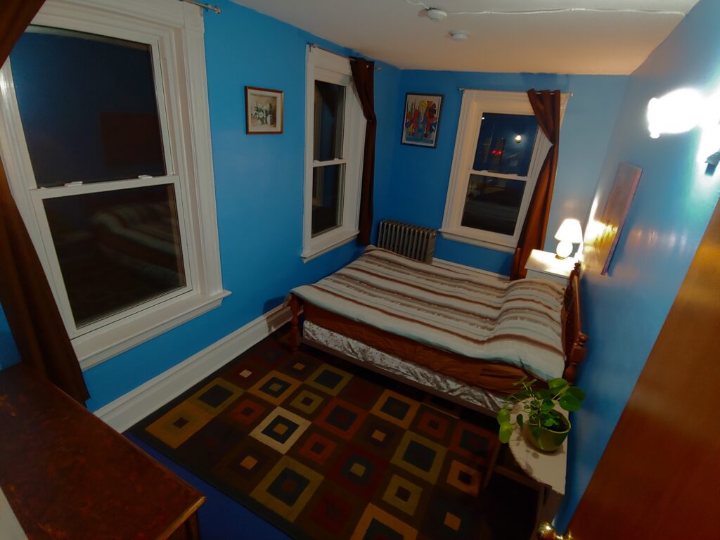 blue room with a double bed, desk & night table - the brown carpet has squares within squares - it's nighttime outside