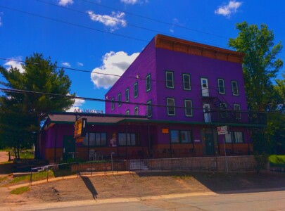 Purple three-story building, aka The Arlington, under blue skies and fluffy clouds