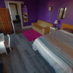 queen bed, couch, night table, two mirrors, wardrobe, tiny desk & chair, pink rug, purple walls